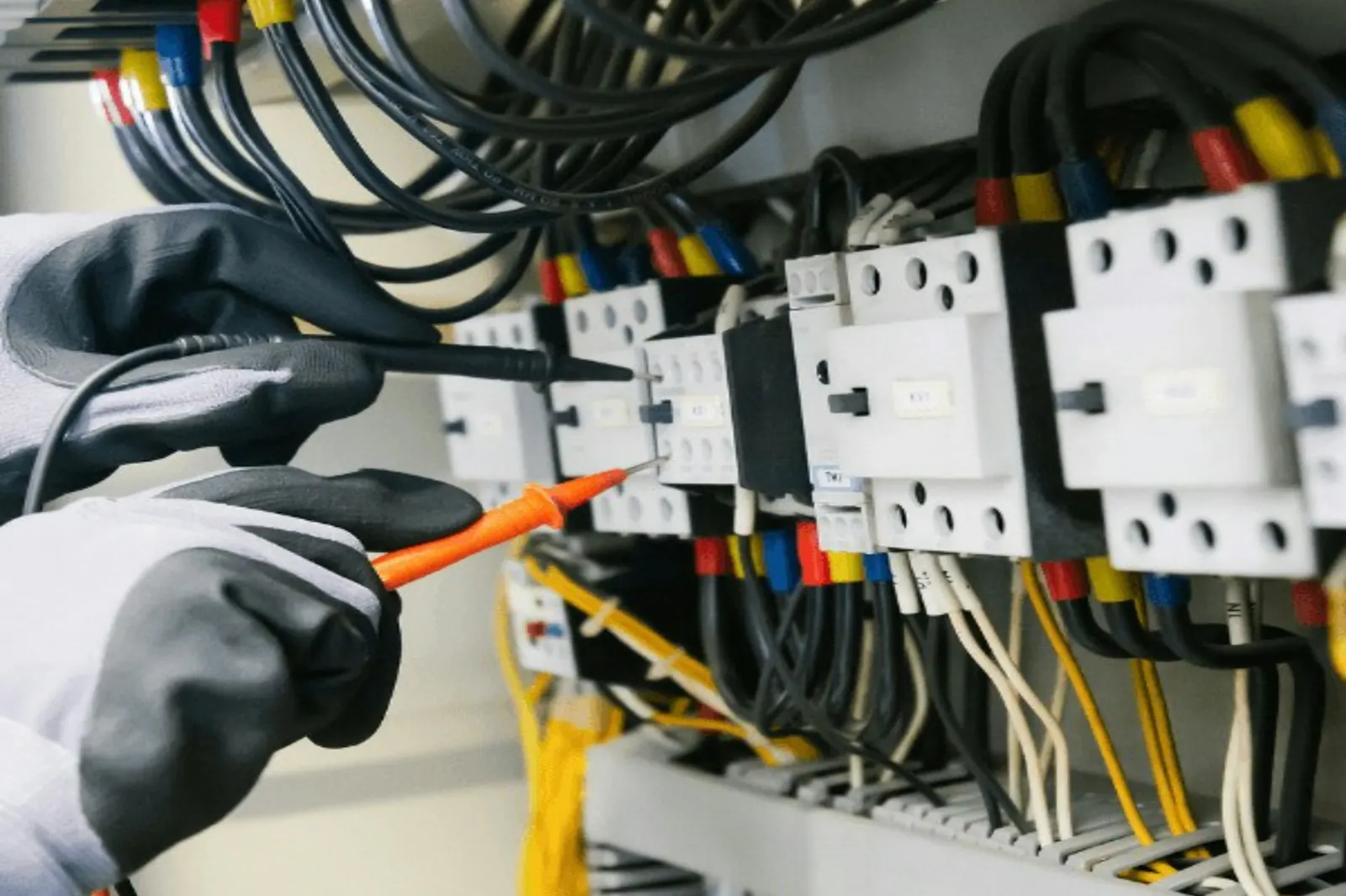 Handschoenen en een spanningstester aan een kast met gekleurde draden